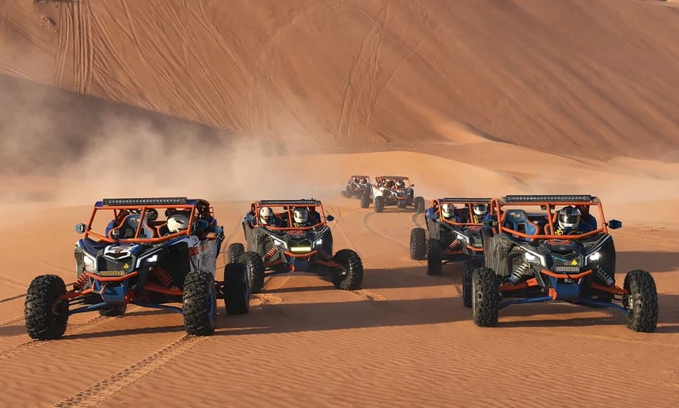 Convoy of off-road dune buggies racing across the sand on a Dubai desert adventure